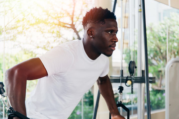 Muscular African American sportsman doing cable fly with exercise machine standing against window during training in gym.