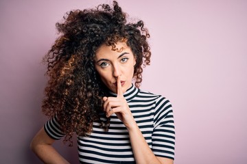 Fototapeta na wymiar Young beautiful woman with curly hair and piercing wearing casual striped t-shirt asking to be quiet with finger on lips. Silence and secret concept.