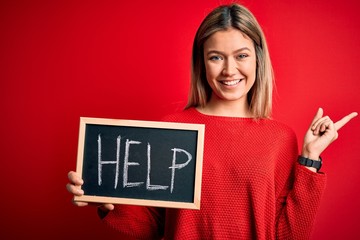 Young beautiful woman holding blackboard standing over isolated red background very happy pointing with hand and finger to the side