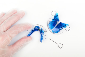 An orthodontist's hand with disposable gloves holds an orthodontic appliance for children on a...