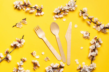 wooden fork, spoon, knife on a yellow background with a sprig of apricot. - Powered by Adobe