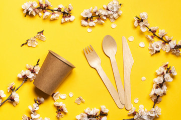 wooden fork, spoon, knife and paper cups on a yellow background with a sprig of apricot.