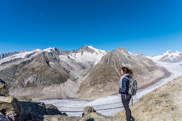 Young Caucasian woman with a backpack on her back looking at the monumental Aletsch Glacier.