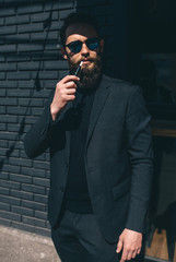 Electronic Cigarette Technology. Handsome man with beard in trendy formal suit smoking an electronic cigarette. Tobacco heating system.