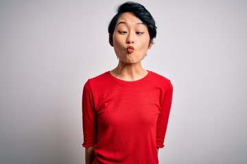 Young beautiful asian girl wearing casual red t-shirt standing over isolated white background making fish face with lips, crazy and comical gesture. Funny expression.