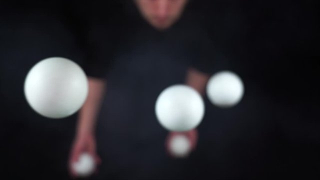 Circus artist wearing black juggling with white balls in slow motion