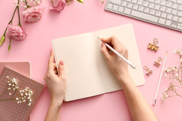Woman writing something in notebook on color background