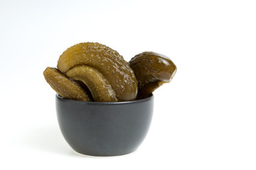 Ugly pickles in a dark bowl on a light background. Close-up, space for text