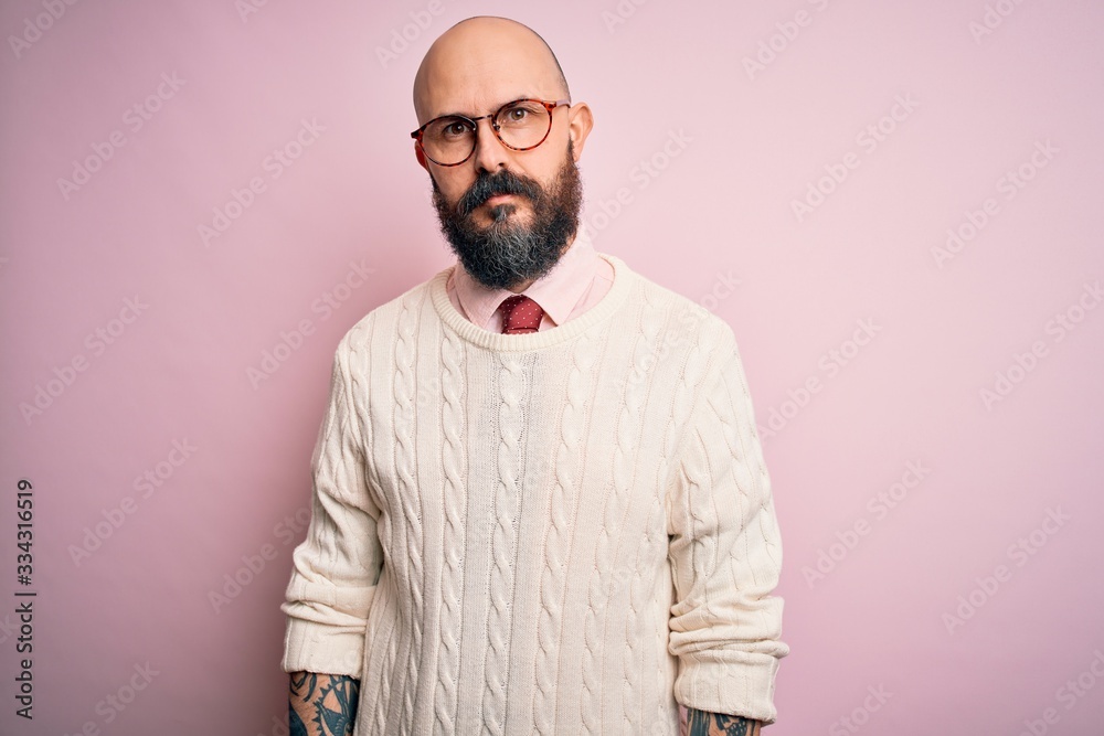 Sticker Handsome bald man with beard and tattoo wearing glasses and sweater over pink background Relaxed with serious expression on face. Simple and natural looking at the camera.