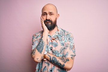 Handsome bald man with beard and tattoo wearing casual floral shirt over pink background thinking...