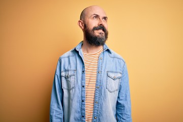 Obraz premium Handsome bald man with beard wearing casual denim jacket and striped t-shirt looking away to side with smile on face, natural expression. Laughing confident.