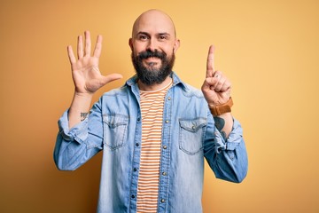 Naklejka premium Handsome bald man with beard wearing casual denim jacket and striped t-shirt showing and pointing up with fingers number six while smiling confident and happy.