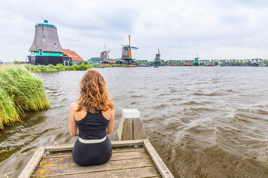 Woman Sitting On Dock Admirs The Windmills In Amsterdam