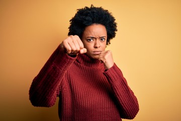 Fototapeta na wymiar Young beautiful African American afro woman with curly hair wearing casual turtleneck sweater Punching fist to fight, aggressive and angry attack, threat and violence