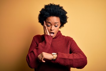 Fototapeta na wymiar Young beautiful African American afro woman with curly hair wearing casual turtleneck sweater Looking at the watch time worried, afraid of getting late