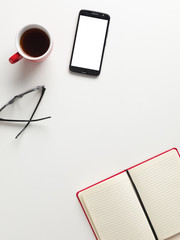 Top view workspace, a blank notebook, mobile, cup of coffee, glasses, white background with space for writing. Top view mockup smartphone white screen