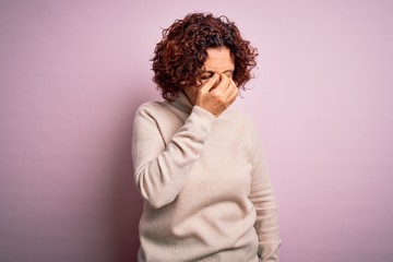 Fototapeta na wymiar Middle age beautiful curly hair woman wearing casual turtleneck sweater over pink background tired rubbing nose and eyes feeling fatigue and headache. Stress and frustration concept.