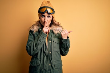 Middle age beautiful blonde skier woman wearing snow sportwear and ski goggles asking to be quiet with finger on lips pointing with hand to the side. Silence and secret concept.
