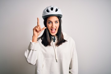 Young cyclist woman with blue eyes wearing bike helmet over isolated white background pointing finger up with successful idea. Exited and happy. Number one.