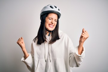 Young cyclist woman with blue eyes wearing bike helmet over isolated white background very happy and excited doing winner gesture with arms raised, smiling and screaming for success. Celebration