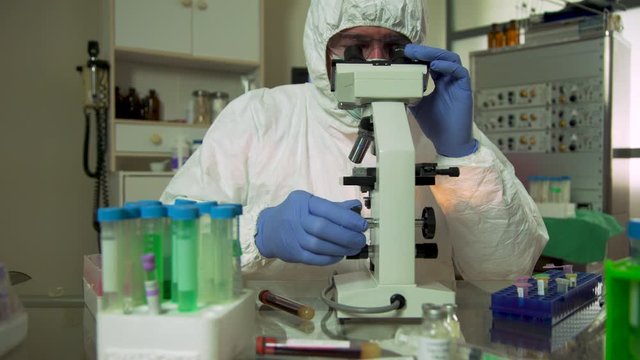 A biomedical research laboratory scientist in full PPE garb working with what must be hazardous viral samples possibly COVID19.