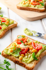 Vegan sandwich with avocado, nuts, vegetables and olive oil on white wooden table