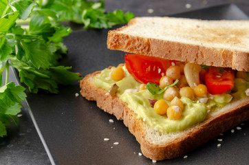 Vegan sandwich with avocado, nuts, vegetables and olive oil on dark background