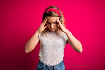 Young beautiful blonde woman wearing casual t-shirt standing over isolated pink background with hand on head for pain in head because stress. Suffering migraine.