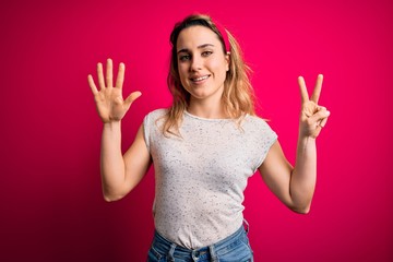 Young beautiful blonde woman wearing casual t-shirt standing over isolated pink background showing and pointing up with fingers number seven while smiling confident and happy.