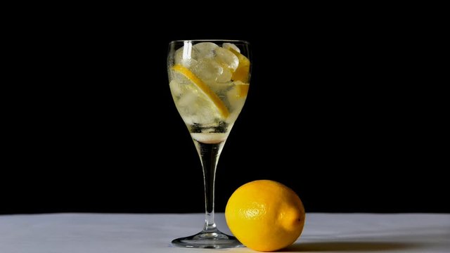 couple cup glasses of sparkling tonic water with ice and lemon, ice melts in time lapse,background black