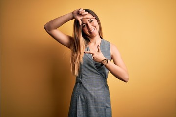 Young beautiful blonde woman with blue eyes wearing dress over yellow background smiling making frame with hands and fingers with happy face. Creativity and photography concept.
