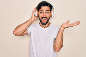 Young handsome hispanic man wearing headphones listening to music over isolated background very happy and excited, winner expression celebrating victory screaming with big smile and raised hands