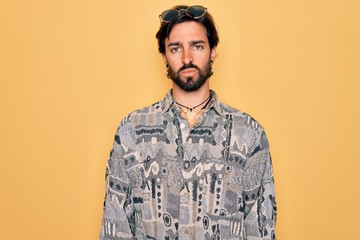 Young handsome hispanic bohemian man wearing hippie style and sunglasses Relaxed with serious expression on face. Simple and natural looking at the camera.