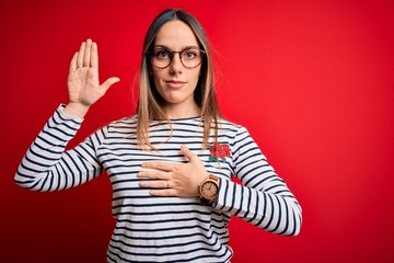 Young beautiful blonde woman with blue eyes wearing glasses standing over red background Swearing...