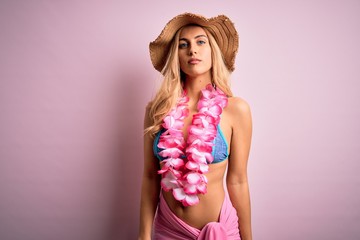 Young beautiful blonde woman on vacation wearing bikini and hat with hawaiian lei flowers Relaxed with serious expression on face. Simple and natural looking at the camera.