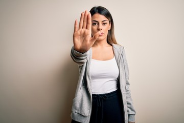 Young beautiful brunette sportswoman wearing sportswoman training over white background doing stop sing with palm of the hand. Warning expression with negative and serious gesture on the face.