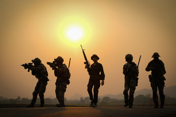 Fototapeta na wymiar Soft blur and silhouette of group of soldier hold the weapon and walk along the road with sunset in the back.