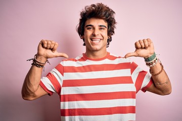 Young handsome man wearing striped casual t-shirt standing over isolated pink background looking confident with smile on face, pointing oneself with fingers proud and happy.