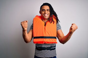 Young african american afro man with dreadlocks wearing orange lifejacket celebrating surprised and...