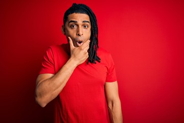 Young handsome african american afro man with dreadlocks wearing red casual t-shirt Looking fascinated with disbelief, surprise and amazed expression with hands on chin