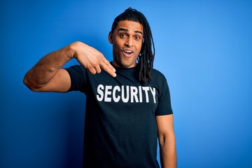 Young african american afro safeguard man with dreadlocks wearing security uniform with surprise...