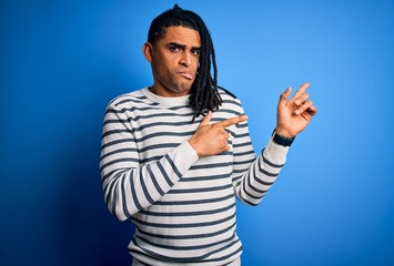 Young handsome african american afro man with dreadlocks wearing casual striped sweater Pointing aside worried and nervous with both hands, concerned and surprised expression