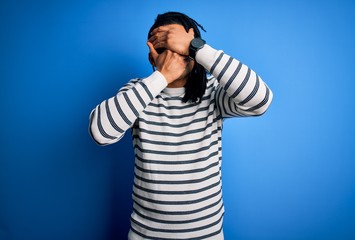 Naklejka premium Young handsome african american afro man with dreadlocks wearing casual striped sweater Covering eyes and mouth with hands, surprised and shocked. Hiding emotion