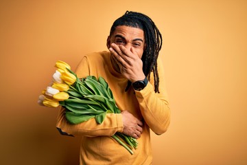 Young african american afro romantic man with dreadlocks holding bouquet of yellow tulips laughing...
