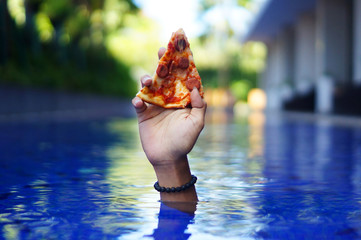 hand holding a slice of pizza on the pool