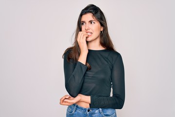 Young beautiful brunette woman wearing casual sweater and jeans standing over isolated background looking stressed and nervous with hands on mouth biting nails. Anxiety problem.