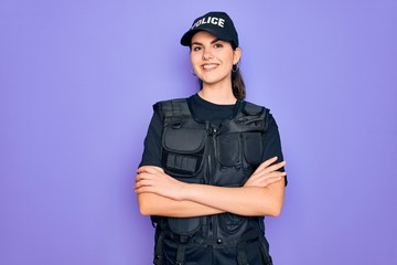Young police woman wearing security bulletproof vest uniform over purple background happy face...