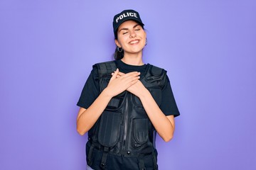 Young police woman wearing security bulletproof vest uniform over purple background smiling with hands on chest with closed eyes and grateful gesture on face. Health concept.