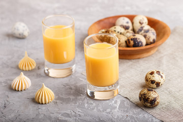 Sweet egg liqueur in glass with quail eggs and meringues on a gray concrete background. Side view