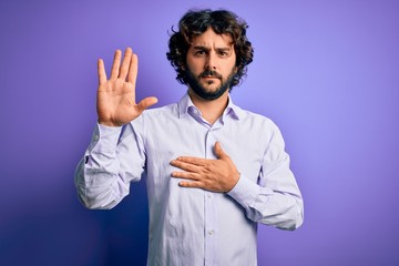 Young handsome business man with beard wearing shirt standing over purple background Swearing with...